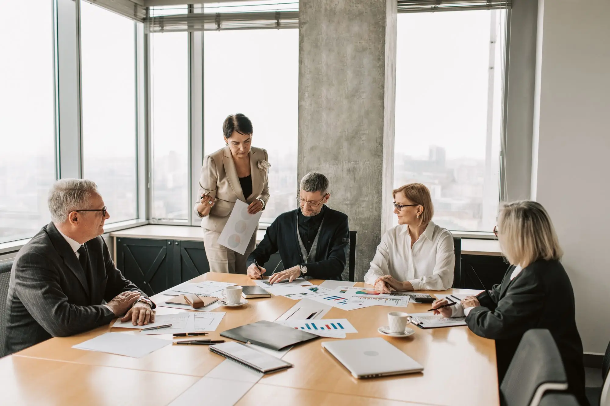 Directors and their adviser reviewing printed financial reports around a boardroom table before a meeting with the bank