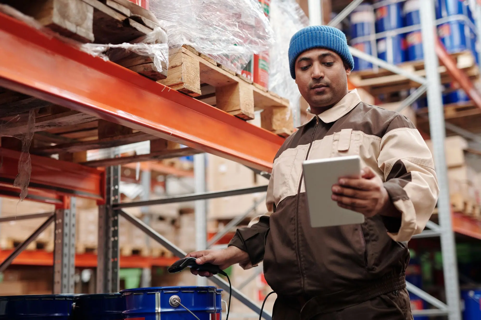 Warehouse supervisor scanning paint tins and checking the count on a tablet during a completion-day stocktake among pallet racking